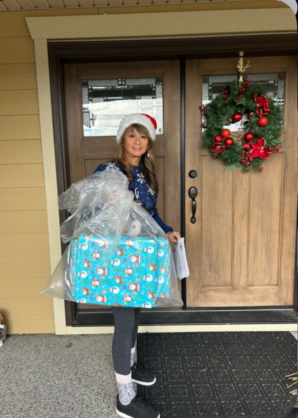 Teresa May in a Santa hat delivering a wrapped Christmas present to a Kelowna doorstep in 2022.